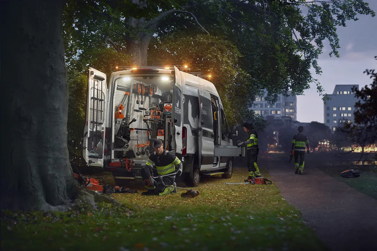 A team working on a van in a park, highlighting the use of Husqvarna Battery Powered Lawn Products