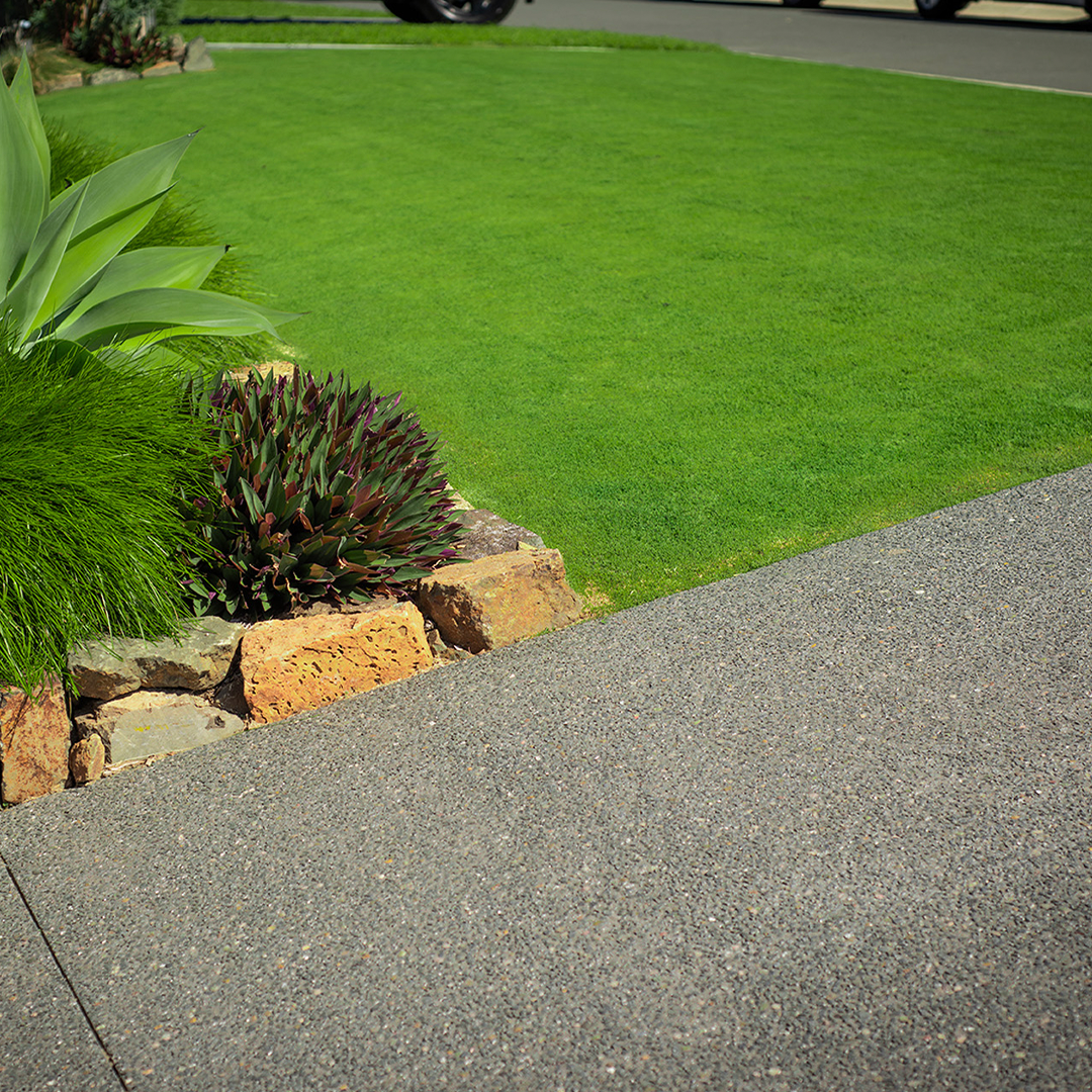 A grassy area featuring TifTuf Bermuda Grass, a flower bed, and a paved sidewalk.